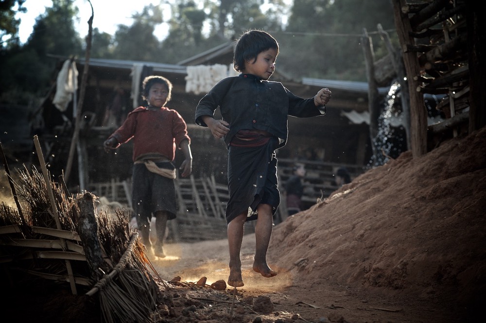 Two boys in evening light  running on a dusty path in an  Eng (Ann)  village near Kyaing Tong (Kentung), Shan State, Myanmar (Burma)